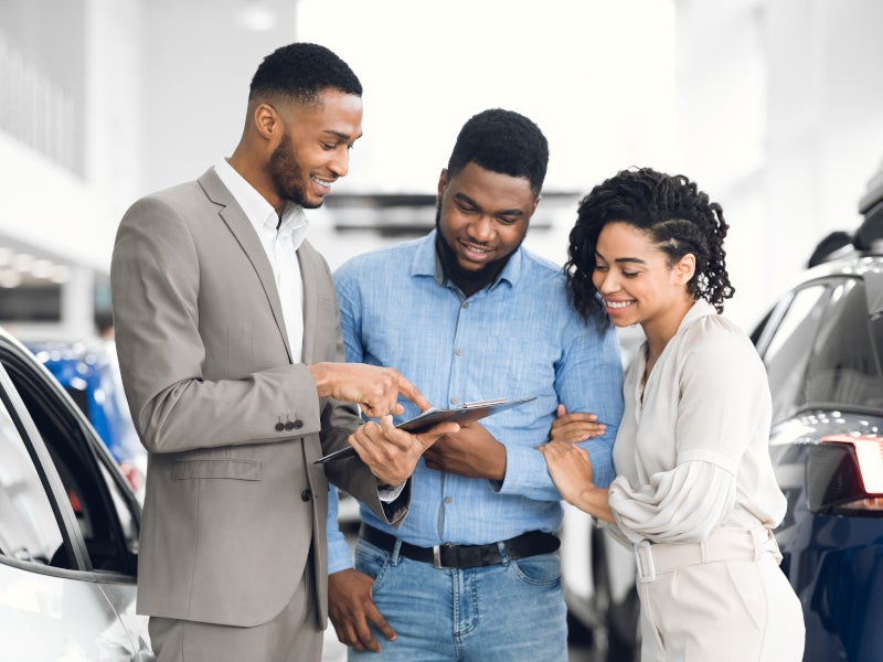 a couple with a sales rep looking at details on a clipboard regarding a vehicle
