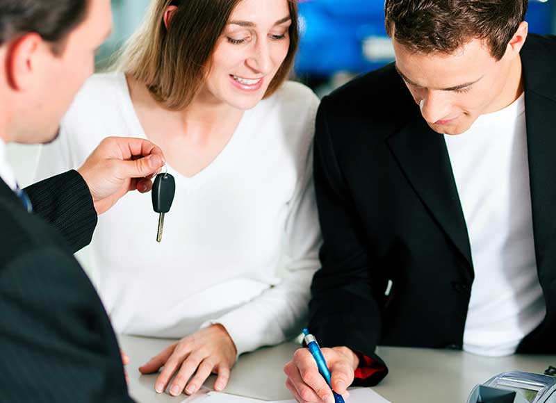 a couple going over financing with a salesman who is holding a set of keys